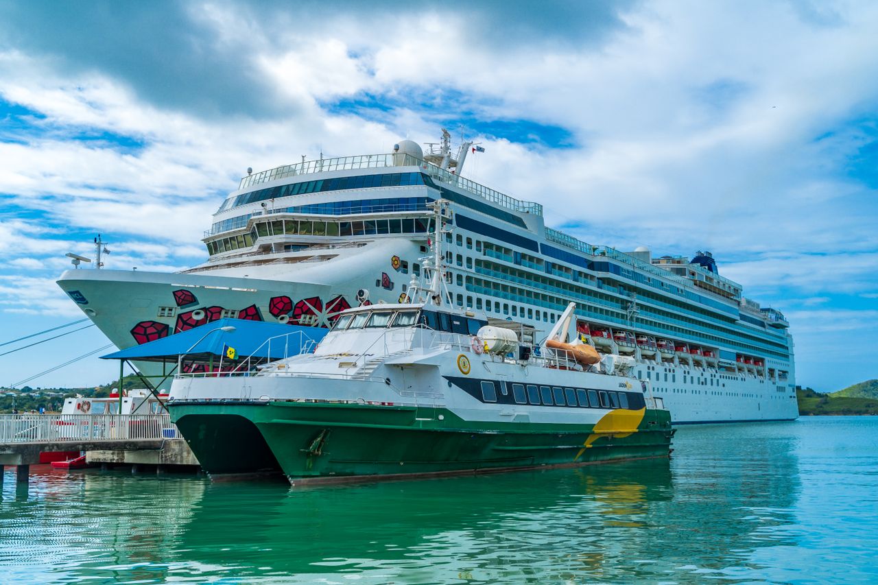 A large cruise ship berthed at a tropical pier with a passenger tender boat moored in front