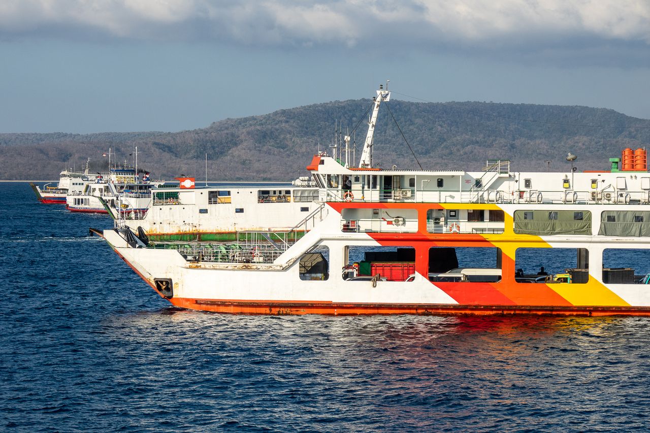Ferries docked at a harbour jetty with forested mountains behind, evocative of a mainland ferry terminal