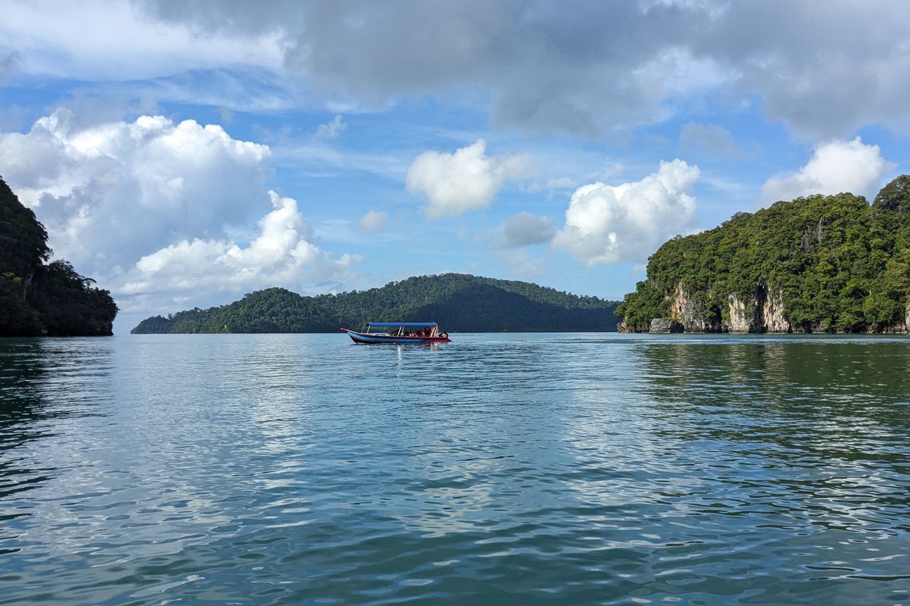 A small tour boat crossing calm water between forested limestone islands in Langkawi