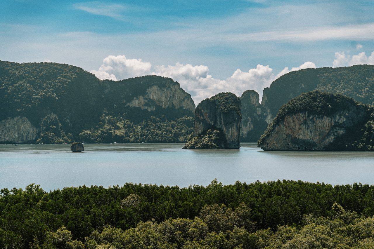 Limestone karst cliffs draped in jungle rising from calm water, evocative of Langkawi's geopark