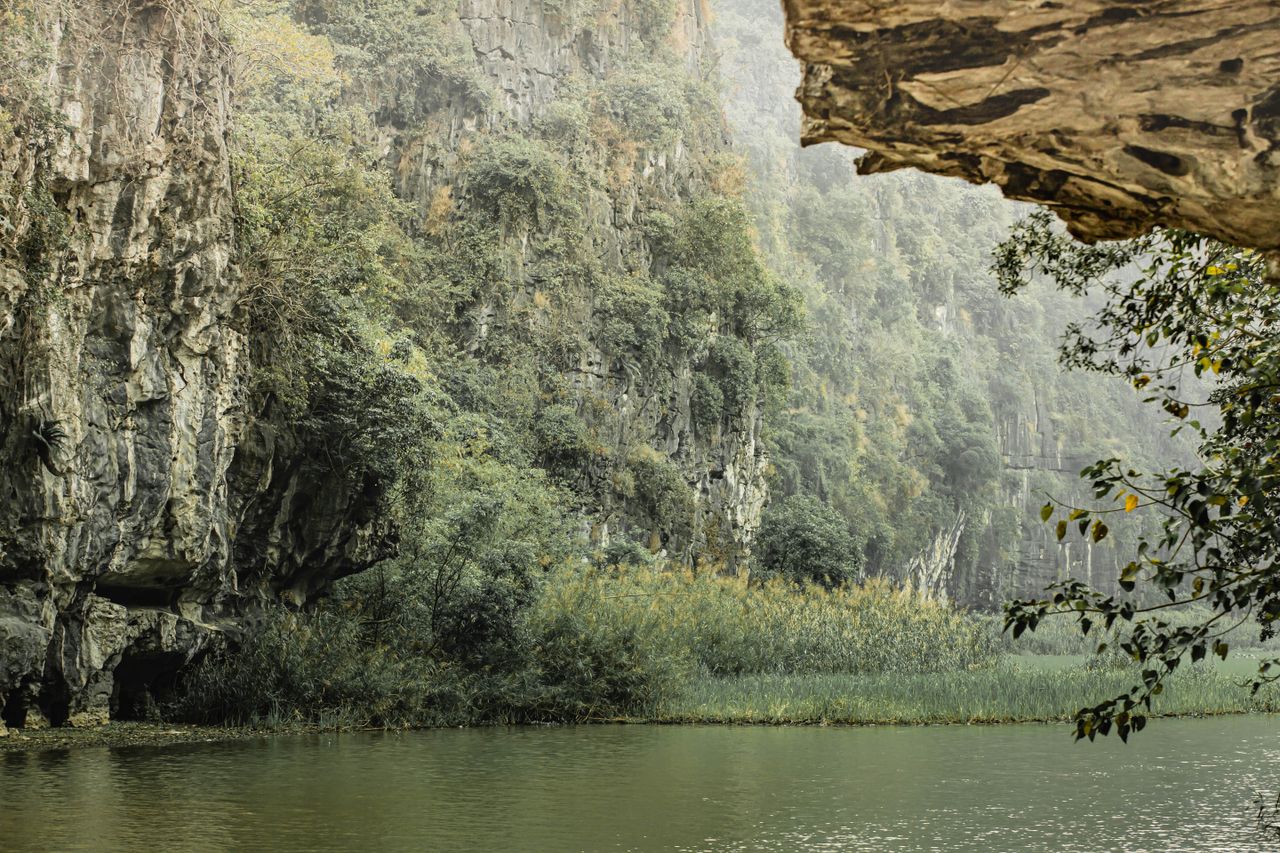 Limestone karst cliffs with a cave overhang rising above calm river water and jungle