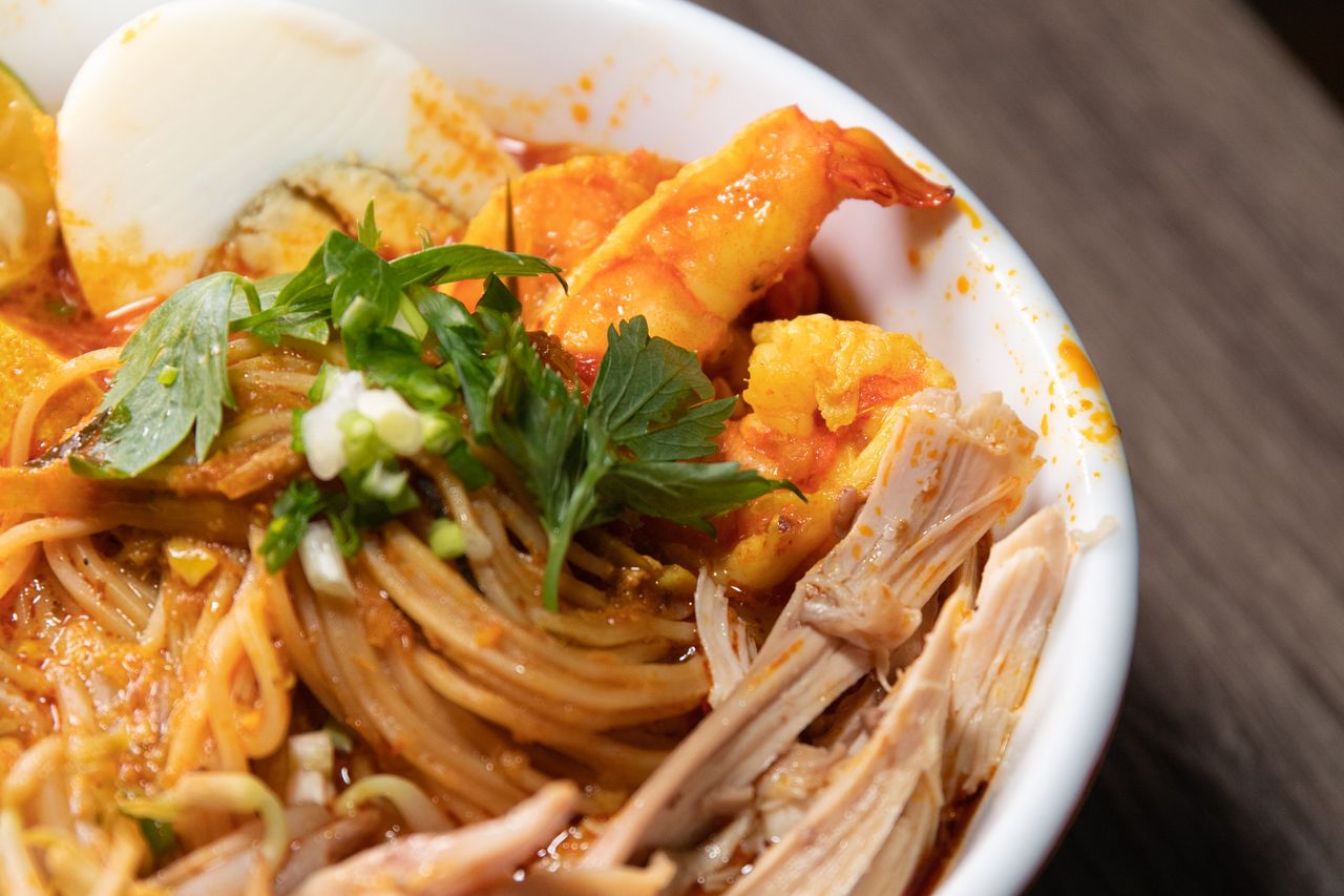 A close-up bowl of Malaysian curry laksa with prawn, shredded chicken, noodles and herbs