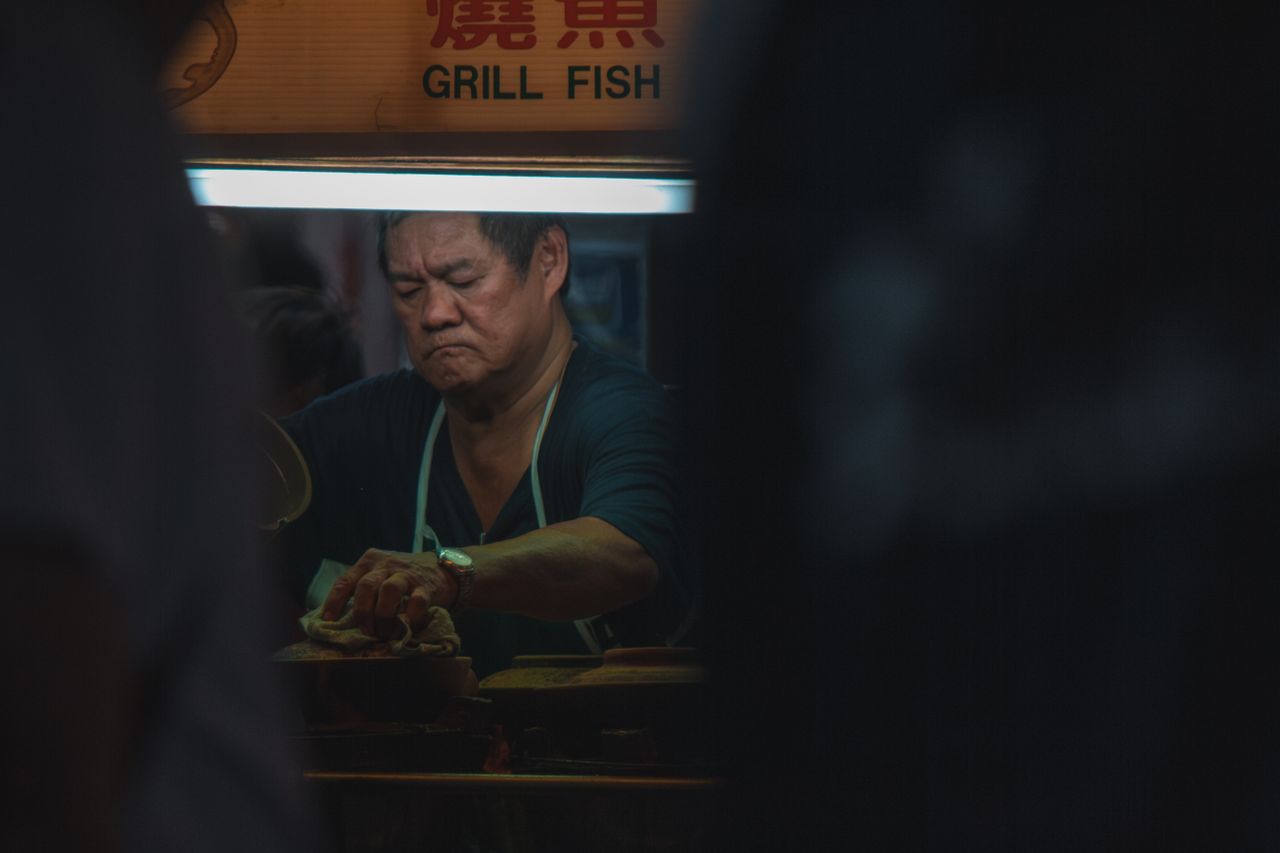 A vendor grilling fish and skewers at a Malaysian night market stall after dark
