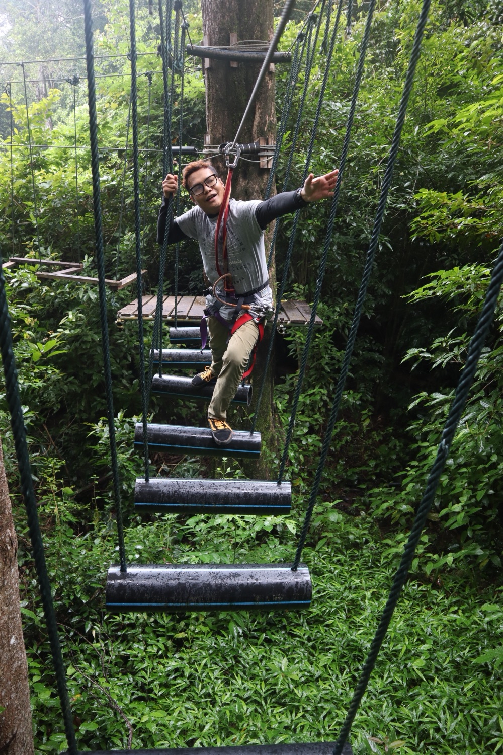 A harnessed visitor balancing across suspended cylinder steps on a high rope bridge at SKYTREX Langkawi